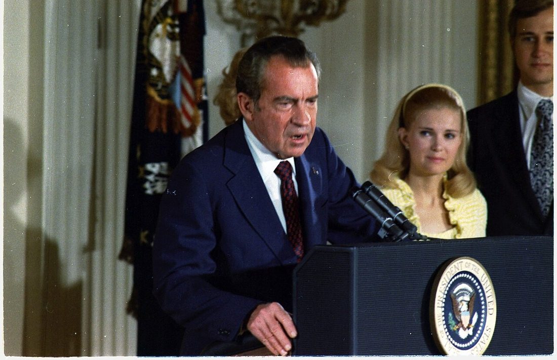 Richard Nixon at a lectern with the presidential seal, addressing White House staff, his daughter beside him.